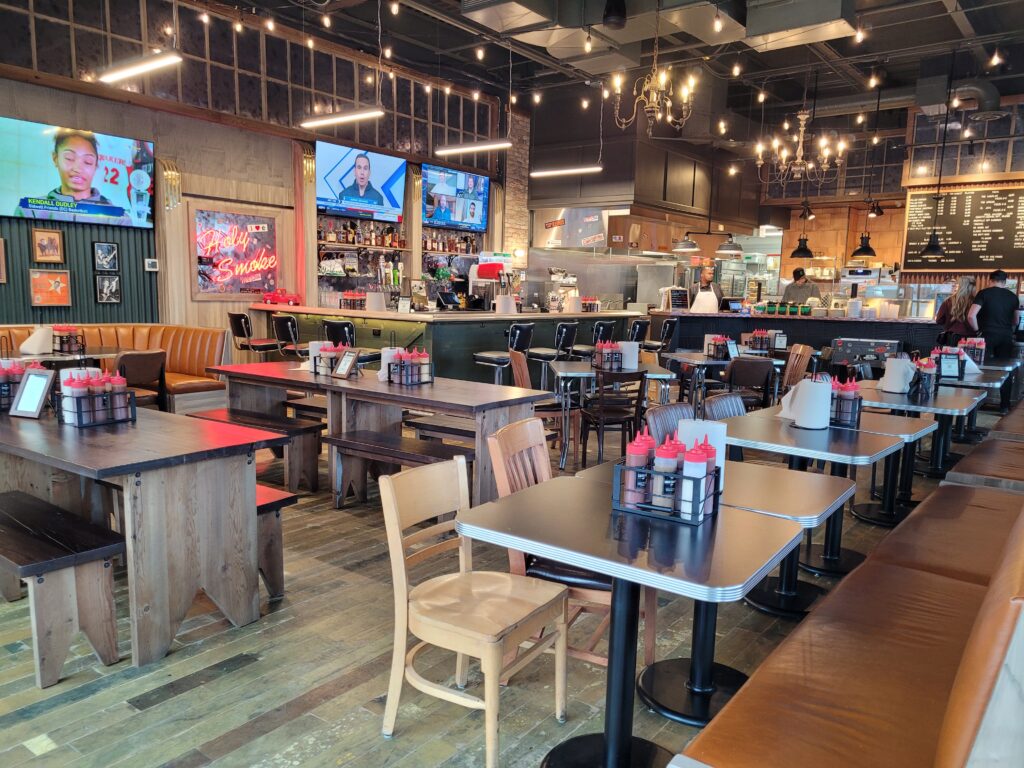 This interior shot of Blackwood BBQ and Catering showcases booths lining the far wall, tables with bench and chair seating, and a long counter that provides additional seating.