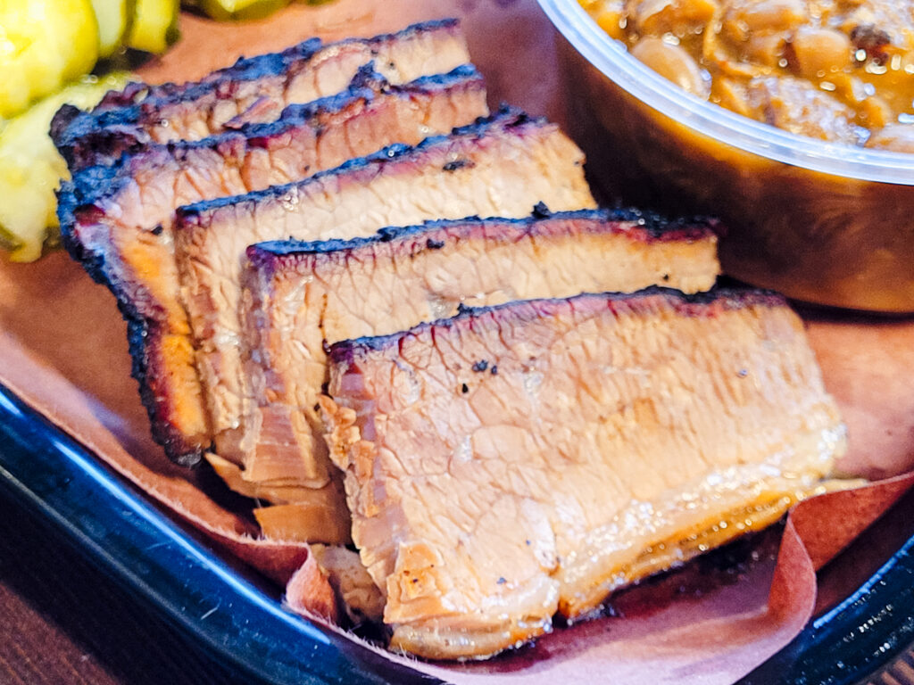 Five slices of brisket overlapping one another on the corner of a paper-lined tray, the tops of each blackened and the surface of the meats marbled with bits of juicy fat.