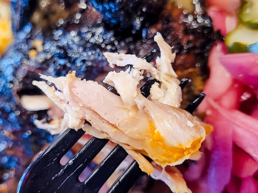A forkful of juicy, white chicken meat glistens in the foreground, with blackened chicken and pickled onions on the plate in the background.