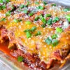 A glass baking dish of cheese enchiladas topped with sliced green onions