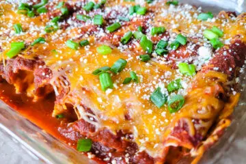 A glass baking dish of cheese enchiladas topped with sliced green onions