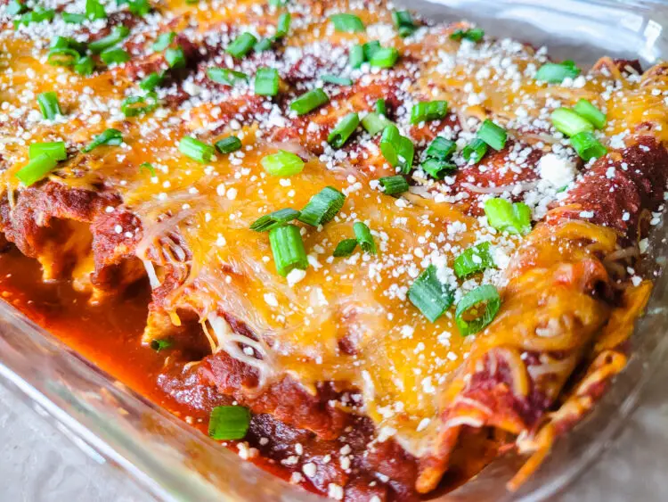 A glass baking dish of cheese enchiladas topped with sliced green onions