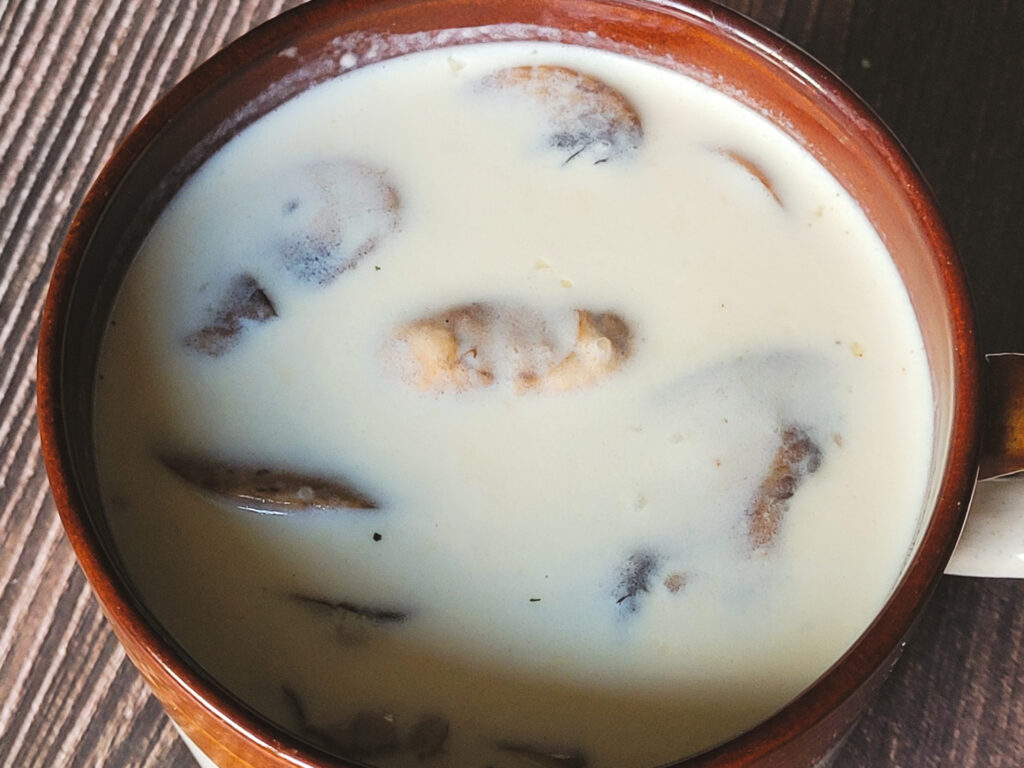 An overhead view of a brown mug of white soup with eight mushrooms visible on top.