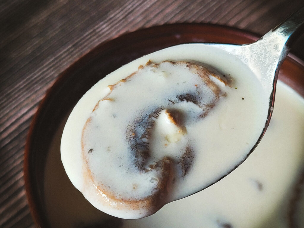 A close-up image of a large mushrooms slice on a spoonful of creamy white soup.