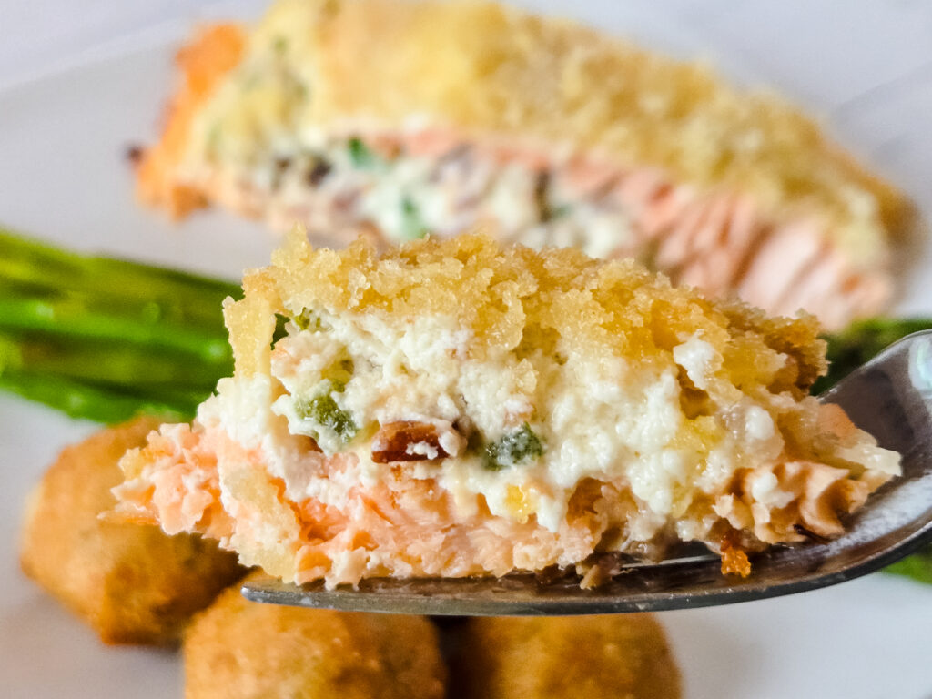 A forkful of jalapeno popper stuffed salmon in side view, featuring a layer of pink, flaky salmon topped with a mixture of cream cheese, bacon, and jalapeno peppers, all topped with crispy panko.